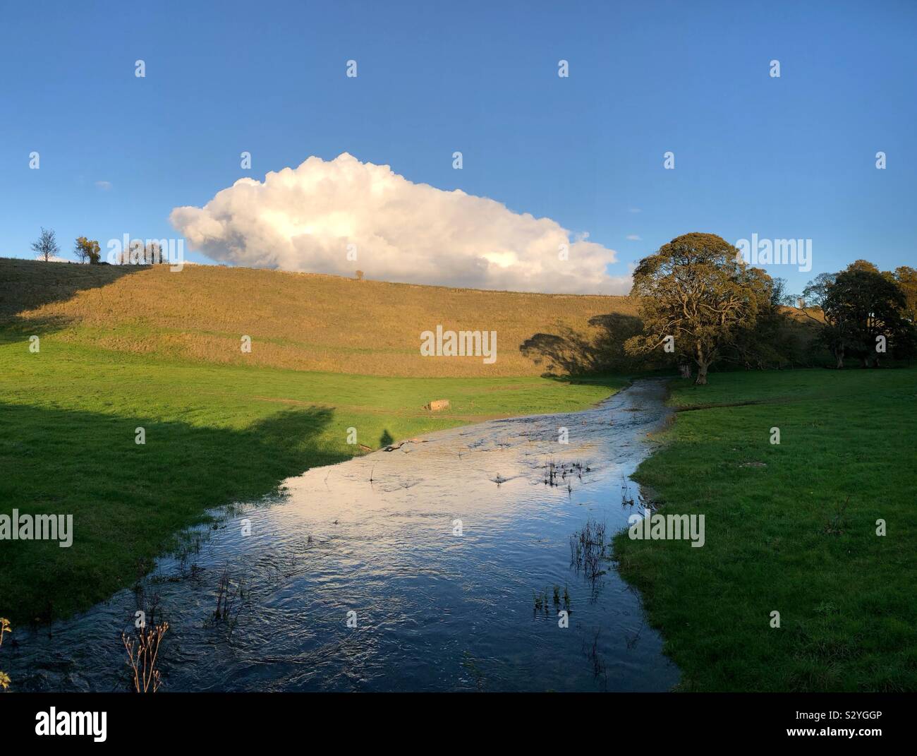 A Cotswold scene of a stream, hill and a cloud apparently resting on top of a ridge. - Smartphone Captured Stock Image