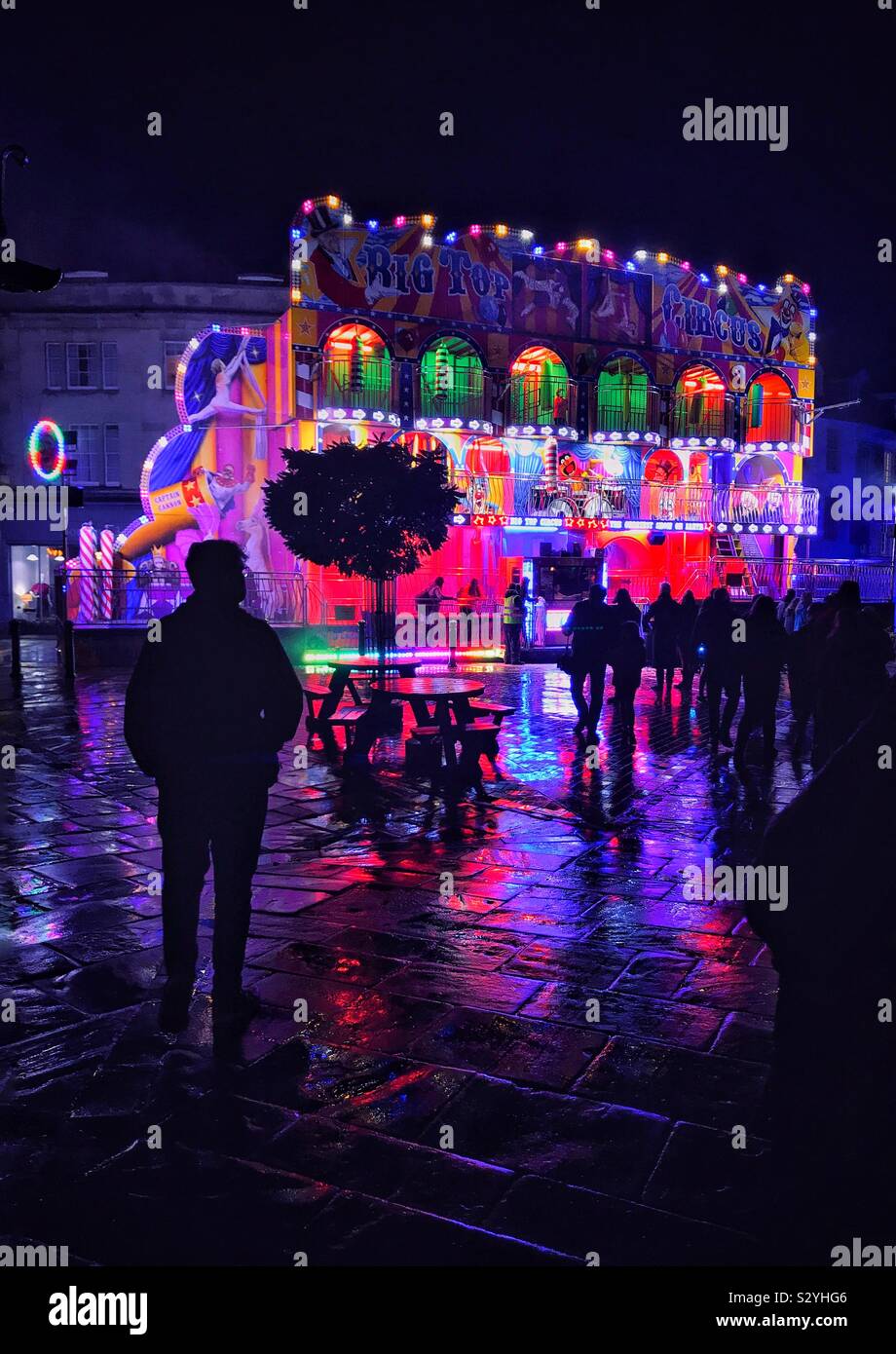 An evening funfair ride at a Fayre somewhere in England. Recent rain means the pavement produces interesting reflected light patterns & colours. Photo Credit - © COLIN HOSKINS. - Smartphone Captured Stock Image
