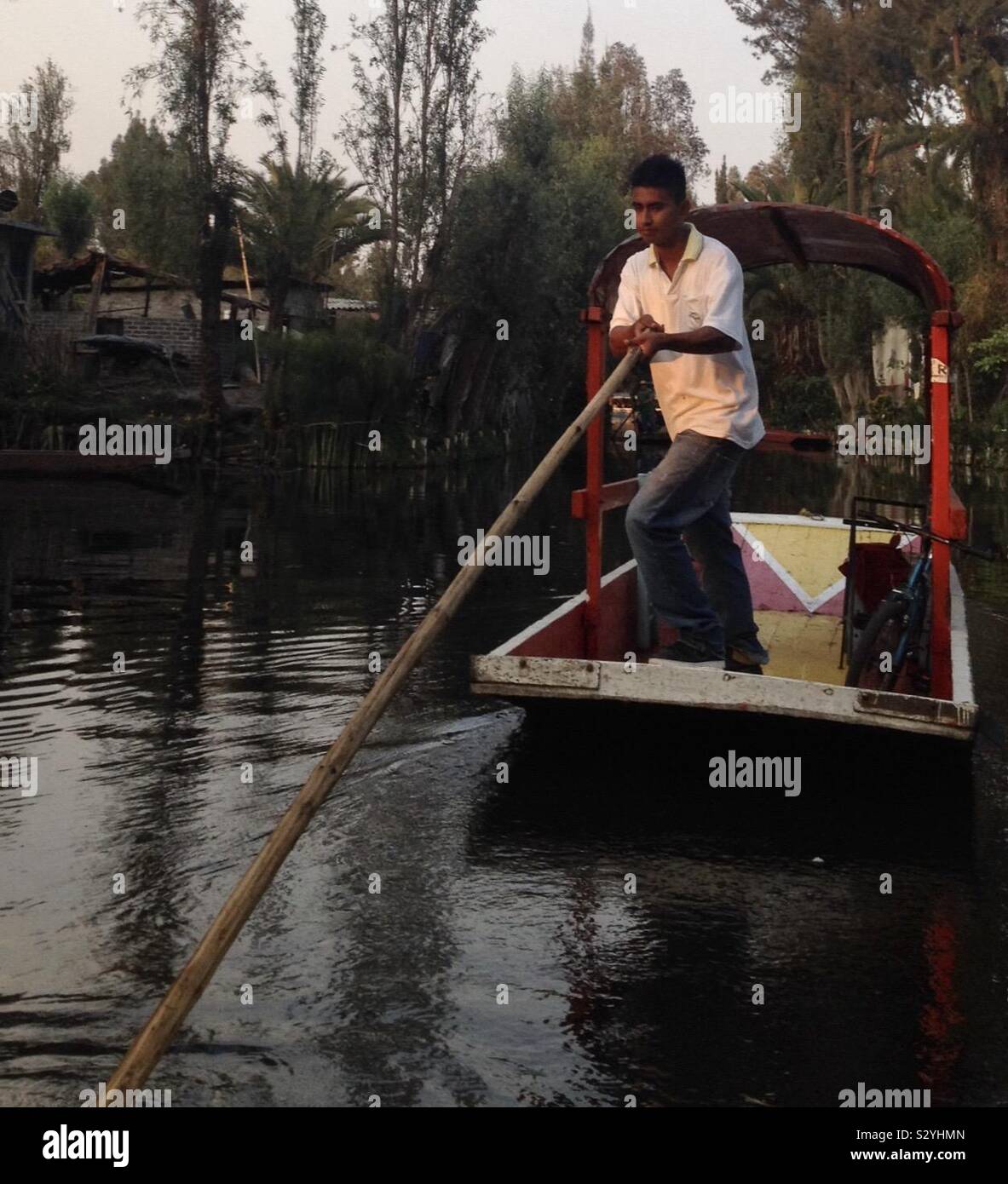 A man uses a pole to steer his trajinera through the canals of Xochimilco, Mexico. Stock Photo