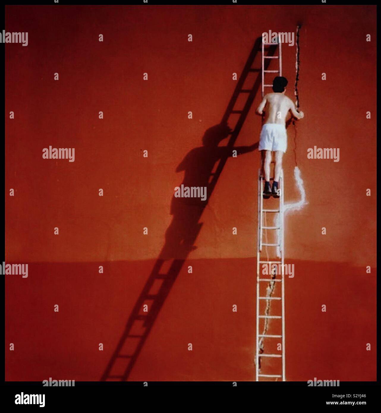 Man on a ladder replastering an orange painted wall - Smartphone Captured Stock Image