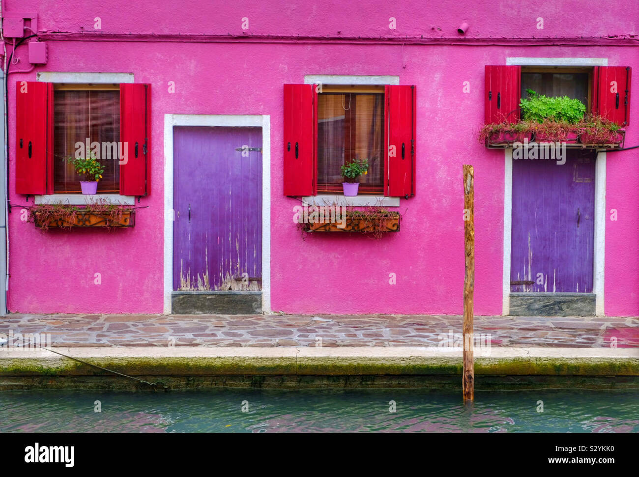 A brightly coloured wall with three windows and two doorways - Smartphone Captured Stock Image