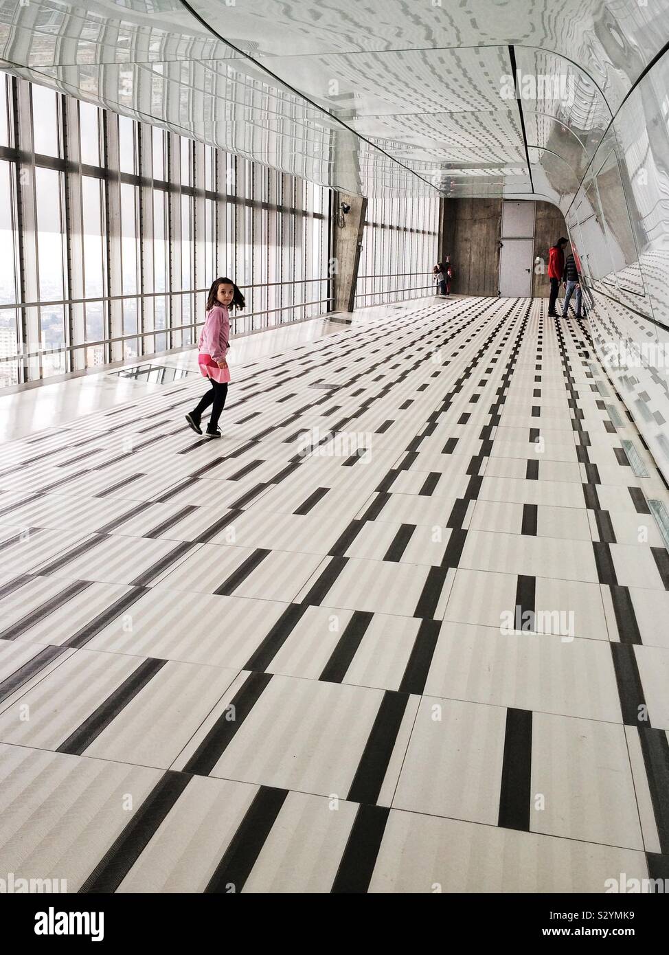Girl wearing pink clothes runs along geometric-patterned floor in Milan’s high-rise Pirelli building Stock Photo