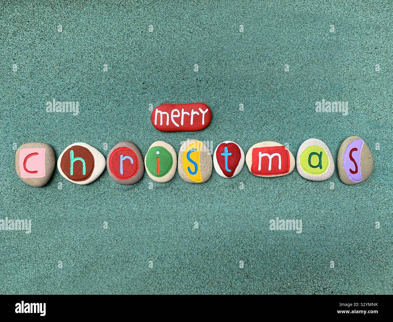 Merry Christmas with a creative composition of colored and carved stones over green sand - Smartphone Captured Stock Image