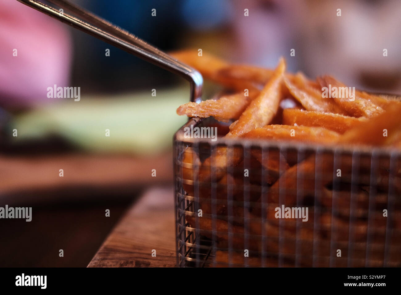 A frying basket full of freshly deep fried sweet potato fries served in