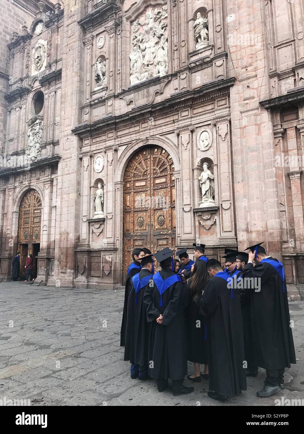 Graduates of the Universidad Michoacana de San Nicolas de Hidalgo gather in their caps and gowns outside the cathedral in Morelia, Mexico, on graduation day. Stock Photo