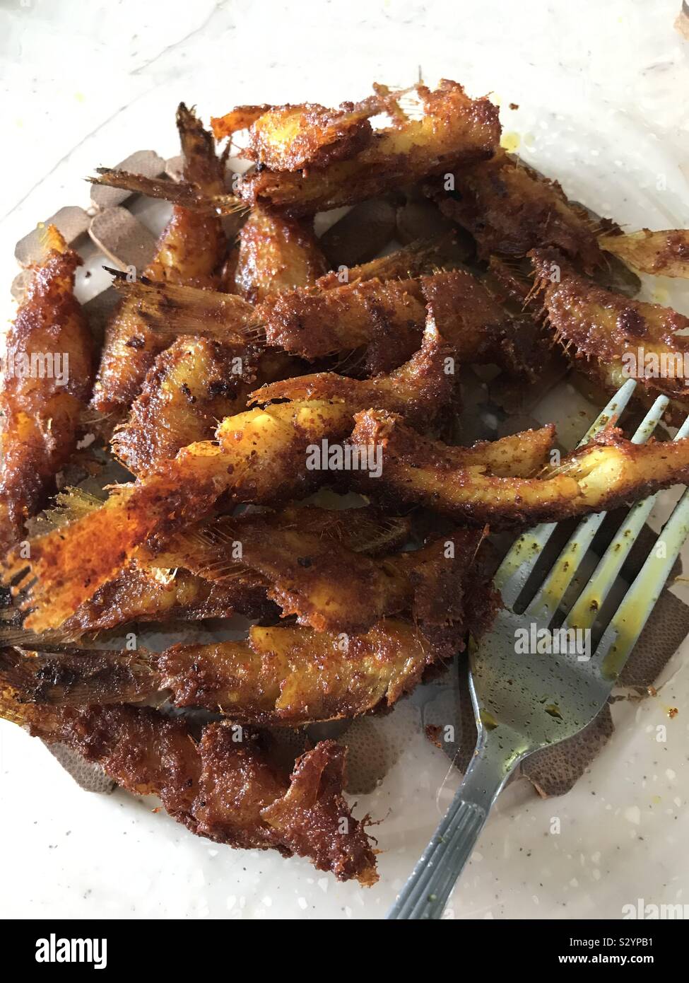 Deep fried spicy smelt fish in a transparent plate with a fork Stock