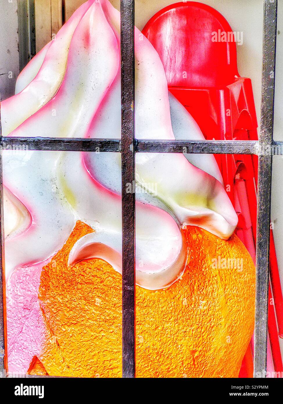 Giant plastic icecream and red plastic chairs behind locked bars in storage for winter, Sweden - Smartphone Captured Stock Image