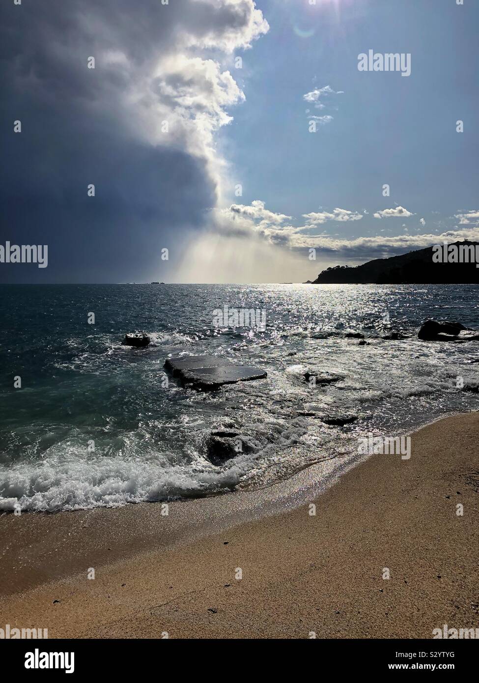 Dramatic rain clouds moving offshore into the Mediterranean Sea and exposing blue sky and sunshine over Canadell beach, Costa Brava in Spain. - Smartphone Captured Stock Image