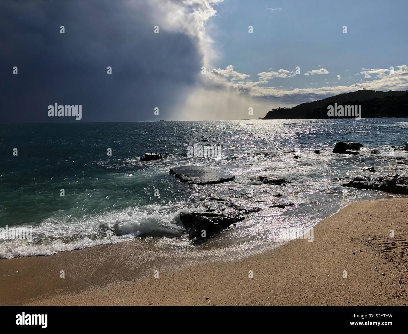 Dramatic rain clouds moving offshore into the Mediterranean Sea and exposing blue sky and sunshine over Canadell beach, Costa Brava in Spain. - Smartphone Captured Stock Image