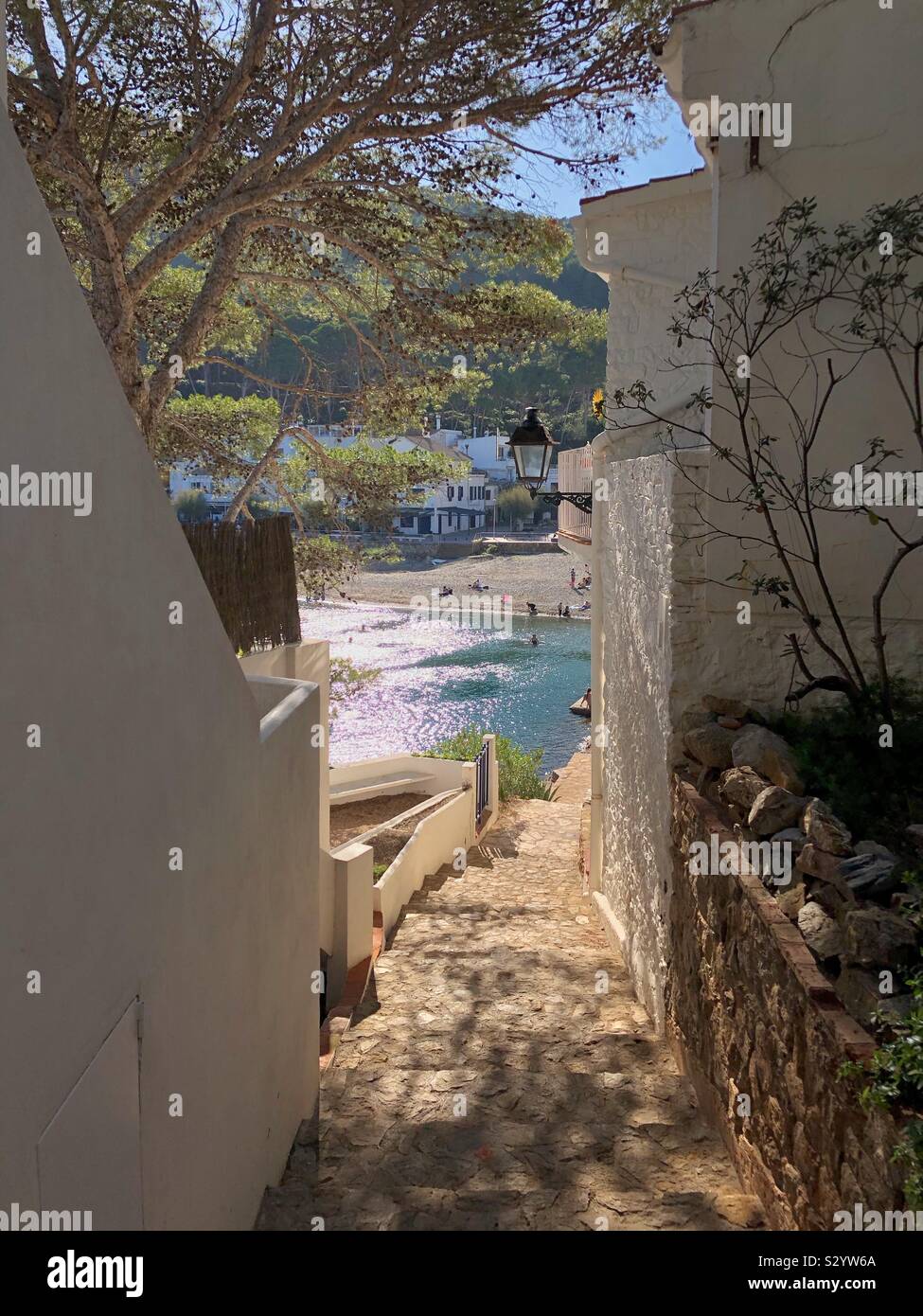 The coastal footpath goes between whitewashed houses down to Sa Tuna beach basking in November sunshine near Begur, Costa Brava in Spain. - Smartphone Captured Stock Image