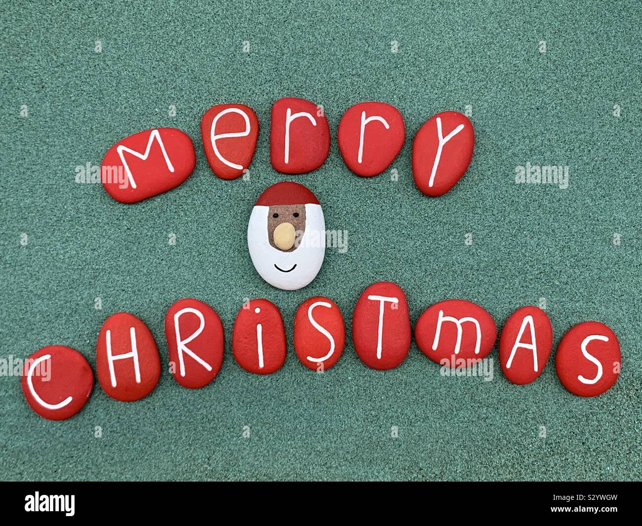 Merry Christmas text with red colred stone letters over green sand - Smartphone Captured Stock Image
