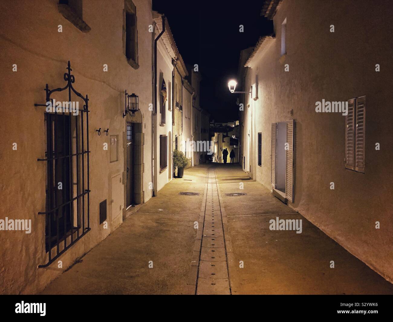 Typical street in the old town of Begur, Spain, at nighttime with three people under the streetlight at the far end. - Smartphone Captured Stock Image