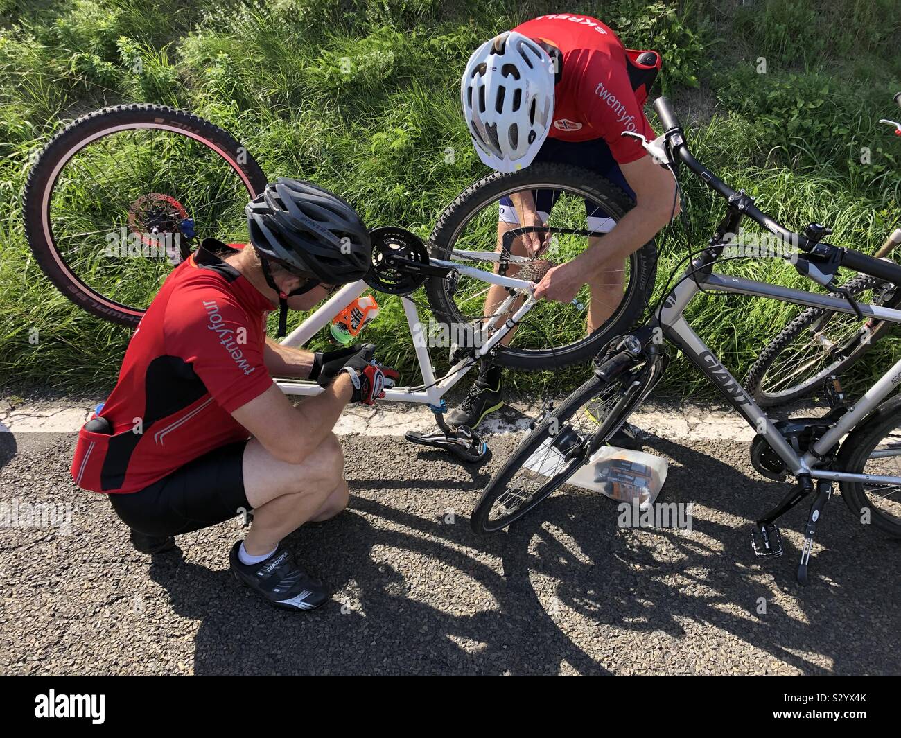 Two cyclists trying to fix a bike with a broken rear derailleur at the roadside in the Moselle Valley, Germany. - Smartphone Captured Stock Image