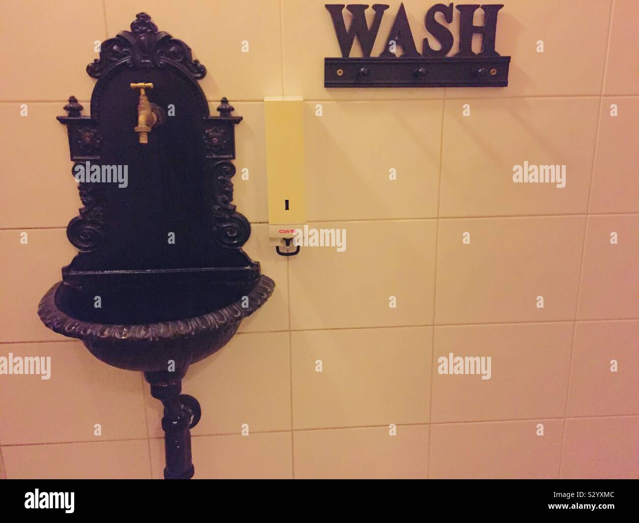 Old fashioned sink in a restaurant’s bathroom. Soap dispenser and wash