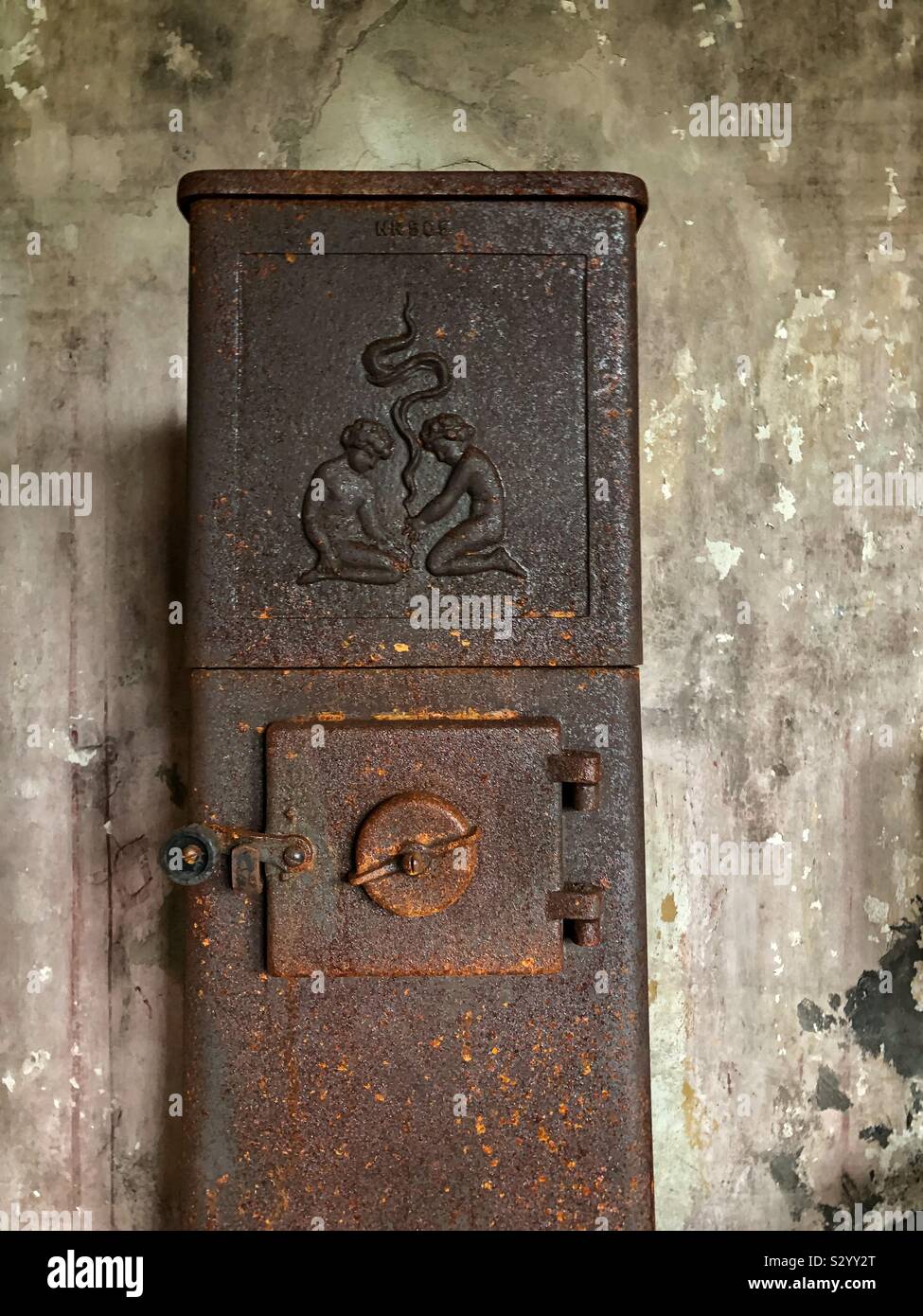 An old, rusty wood burner against an exposed concrete wall in an abandoned farmhouse. Stock Photo