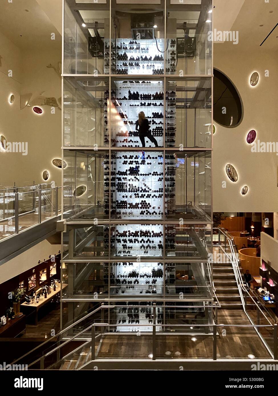 Lady retrieving wine bottles from a large glass wine area - Smartphone Captured Stock Image