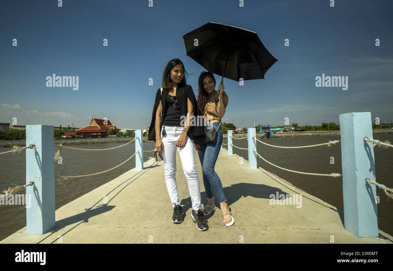 2 Pretty Asian girls in sunshine by sea under umbrella - Smartphone Captured Stock Image