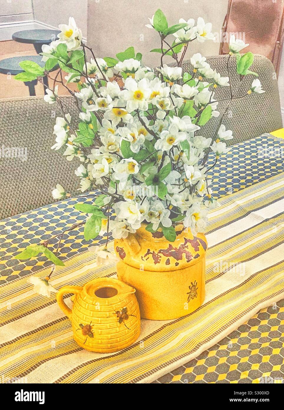 Honeybee themed yellow ware with white silk blossom arrangement Stock Photo
