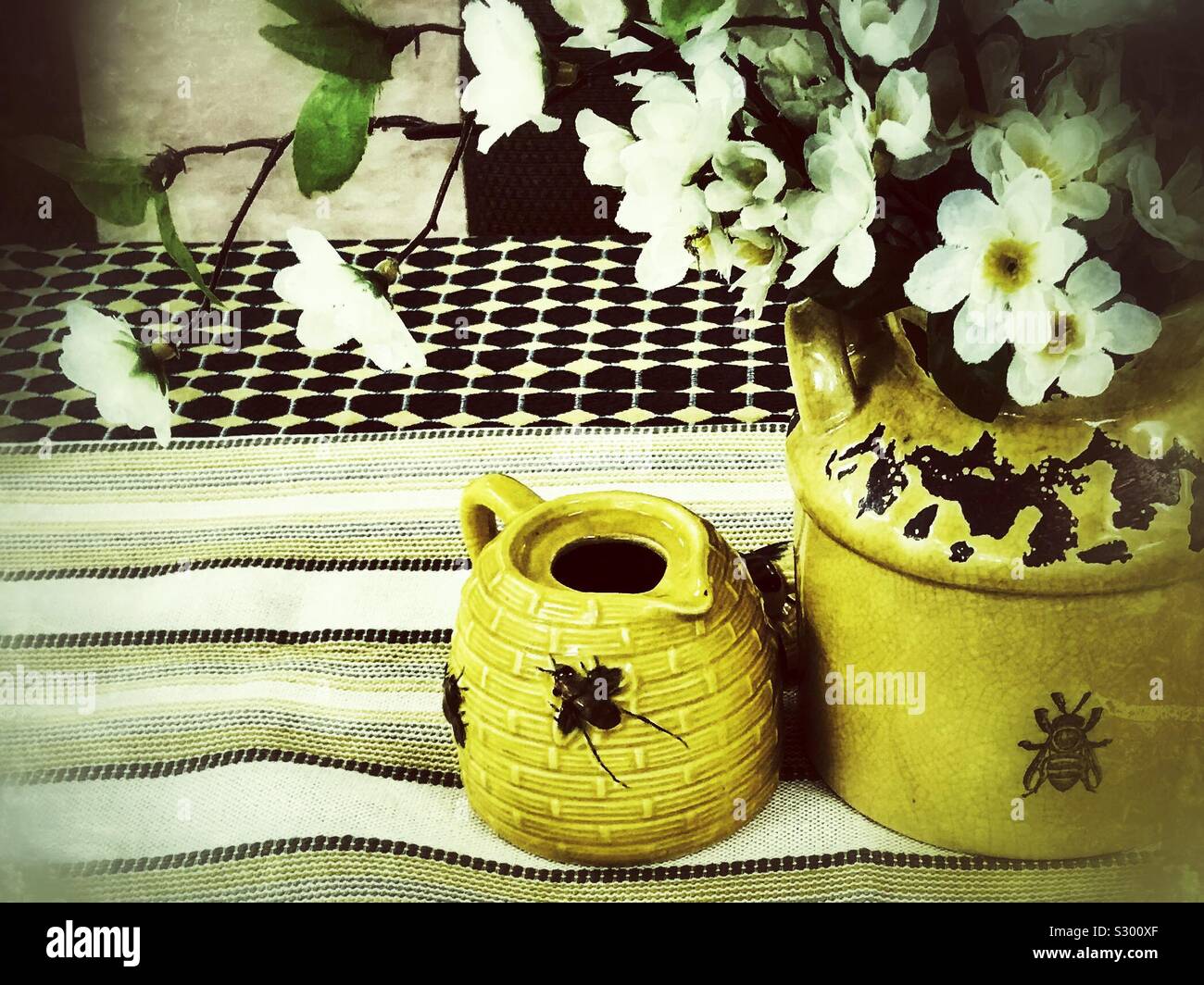 Grunge filtered photo of bee themed yellow ware vases and white silk flower arrangement Stock Photo