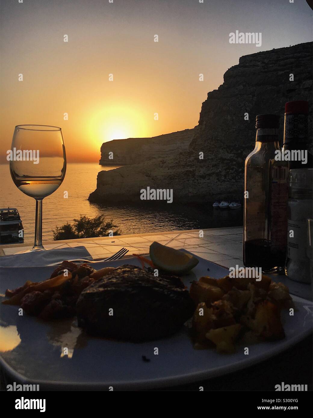 Seaside restaurant with sun setting in background. Xlendi, Gozo, Malta. Stock Photo
