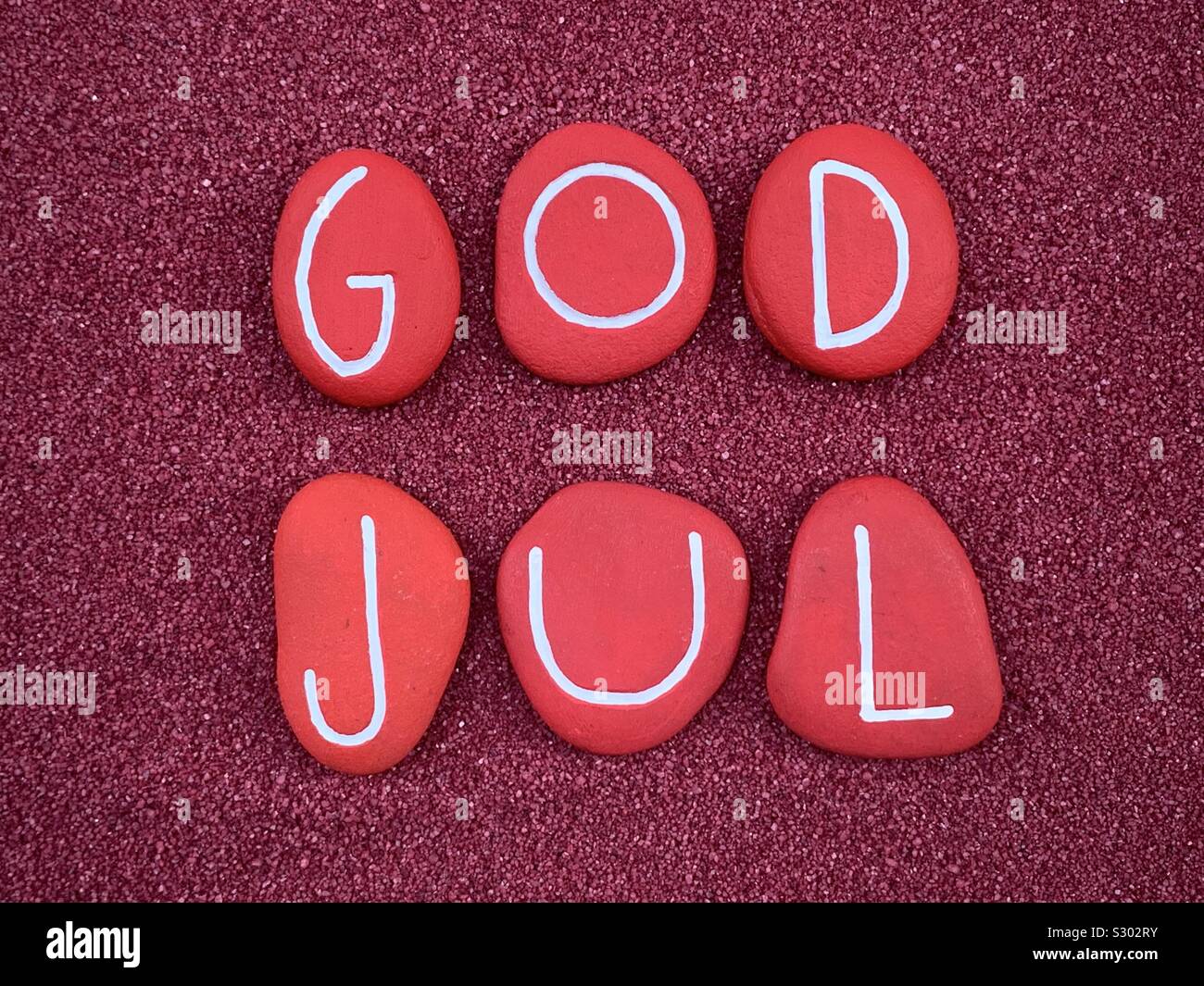God Jul, Merry Christmas composed with red colored and carved stones over red sand - Smartphone Captured Stock Image
