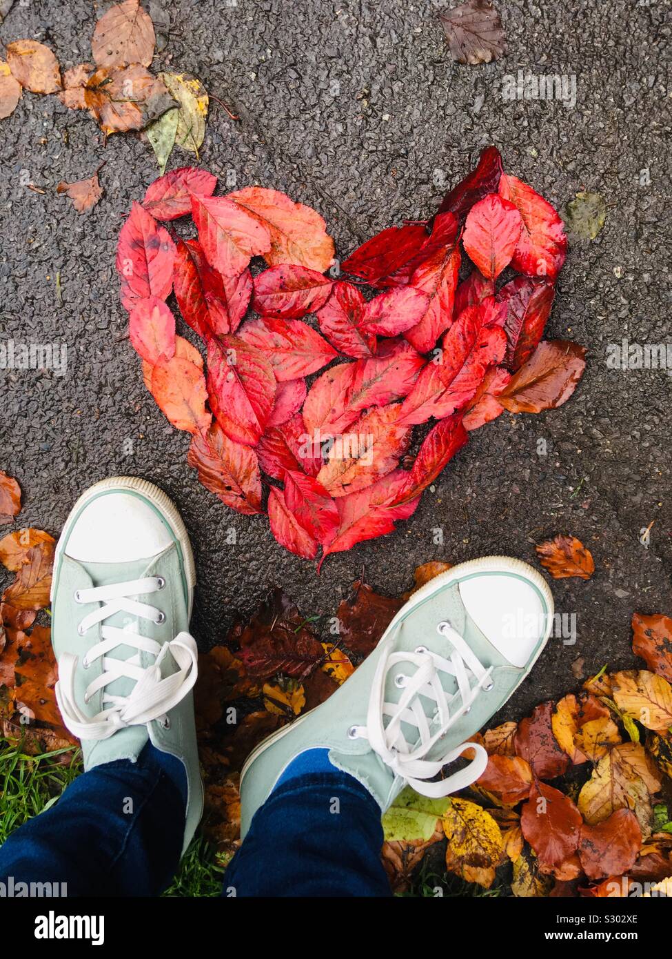 Heart made of leaves on the path with shoes looking down Stock Photo