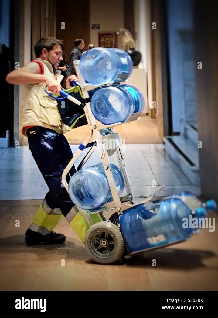 Delivery of bottled mineral water on a trolley by a young man who is carefully balancing the enormous containers Stock Photo