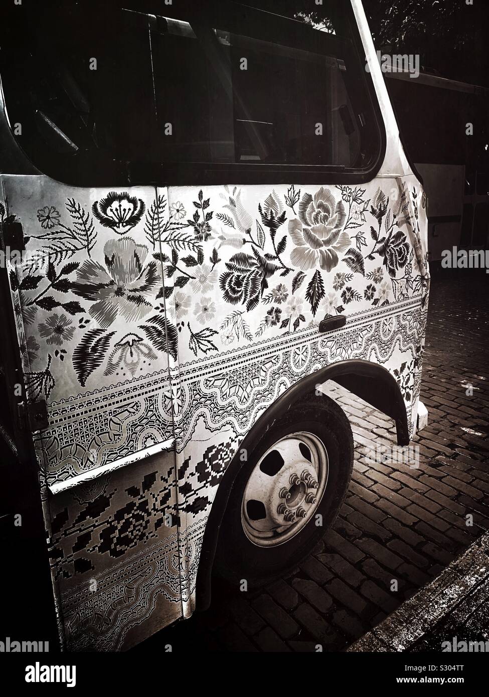 Black and white image of a tour bus painted to look like the local embroidered handicrafts Mérida is known for awaits tourists. Stock Photo