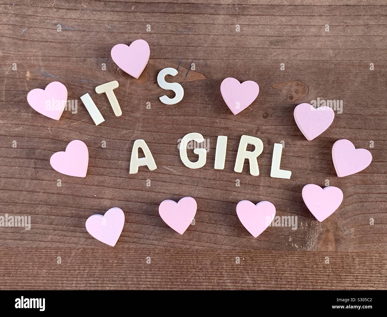 It’s a girl, congratulations message for a new born with wooden letters and pink hearts Stock Photo