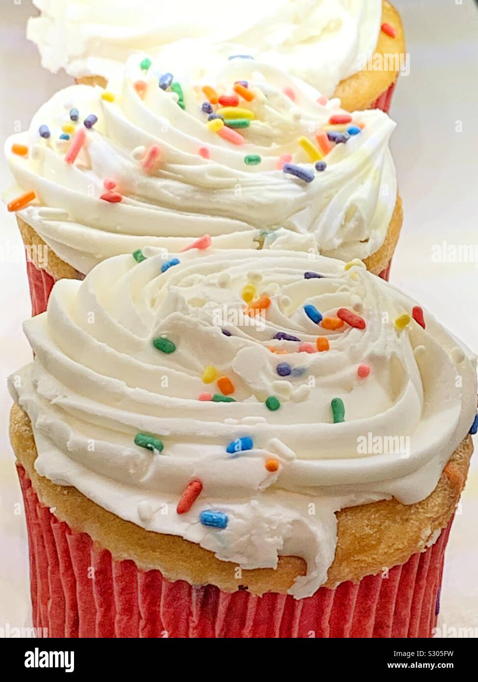 Fresh vanilla cupcakes with white frosting and rainbow sprinkles Stock