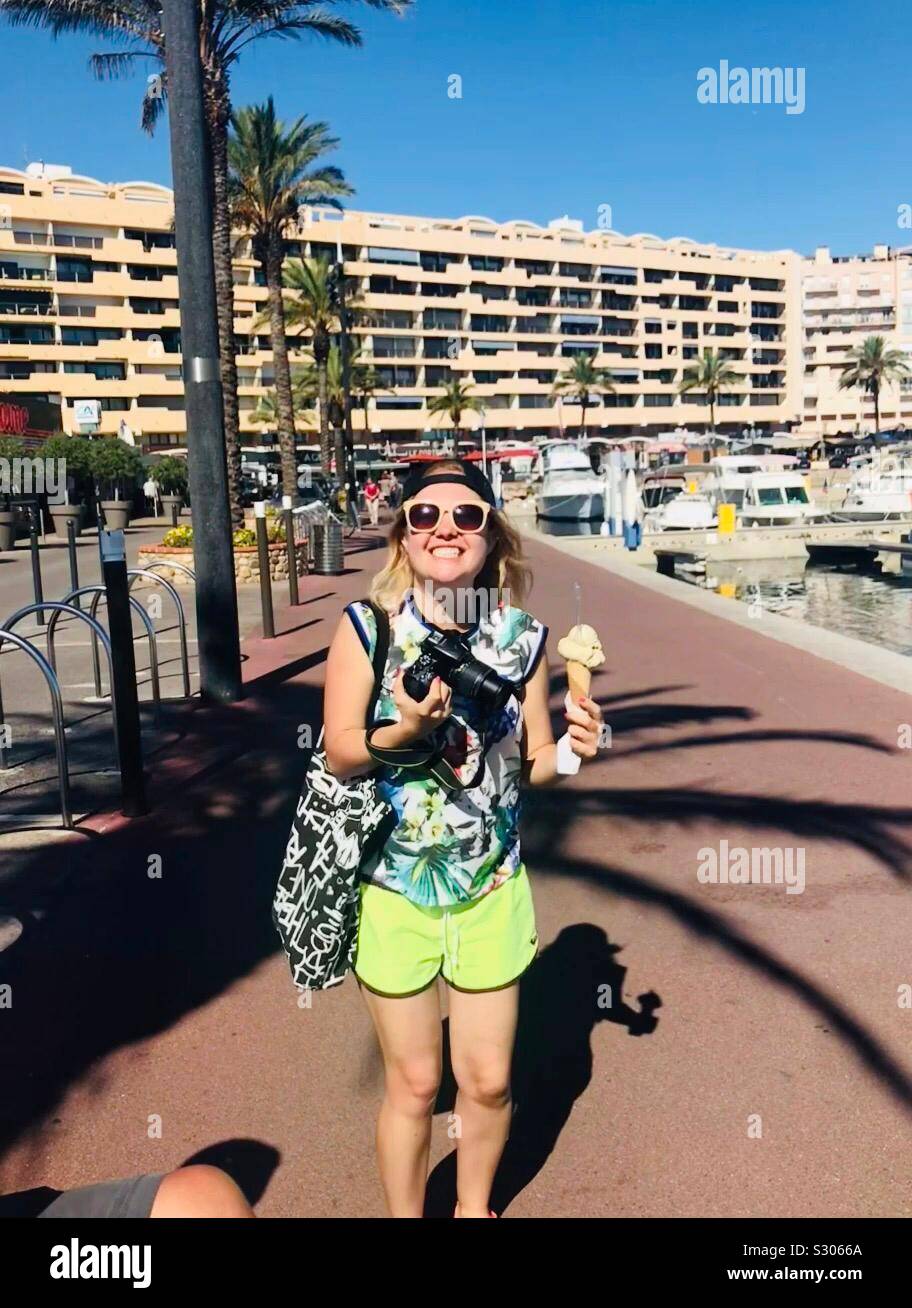 Girl with pistachio ice cream and professional camera in hand.Blond girl with sunglasses on the promenade in the French resort of Saint-Cyprien.Female travel photographer. - Smartphone Captured Stock Image