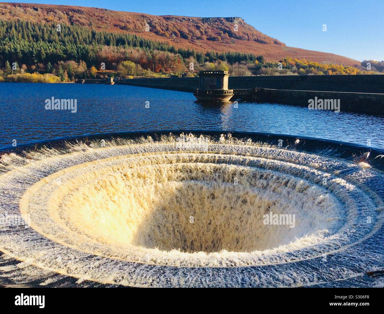 Ladybower reservoir bellmouth overflows or plugholes after heavy rain in November 2019 with autumn colours on hillside Bamford Derbyshire England UK GB Europe Stock Photo