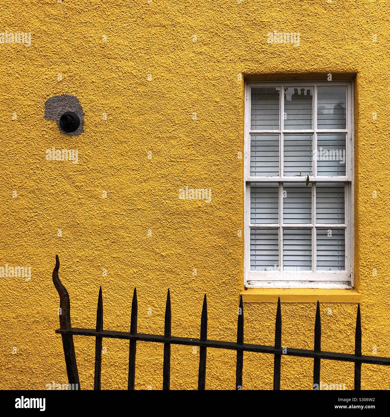 Railings against a yellow roughcast wall with boiler vent, window and closed Venetian blinds - Smartphone Captured Stock Image