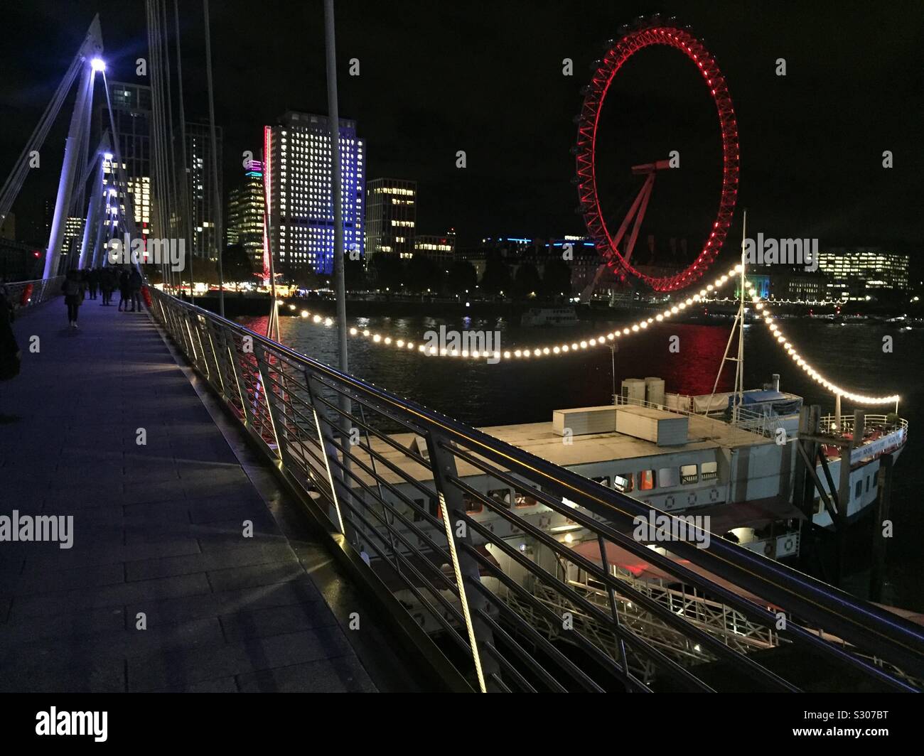 Waterloo bridge at night. City life in central London. Commuters walking over bridge to and from the station of the underground.London Eye at the background. - Smartphone Captured Stock Image