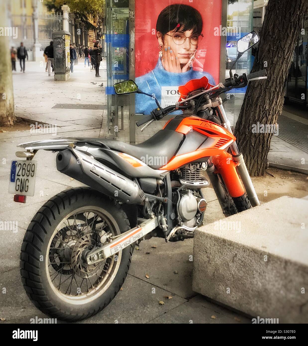 A motor bike is parked on the pavement in front of a bus shelter on which there is a photo of a woman in an advertisement Stock Photo