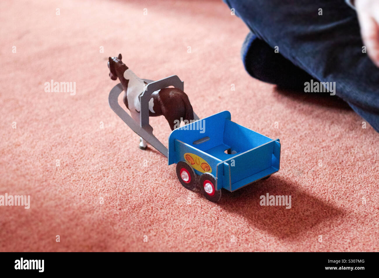 Play Horse with pendant on a terracotta carpet floor in front of a child's leg Stock Photo