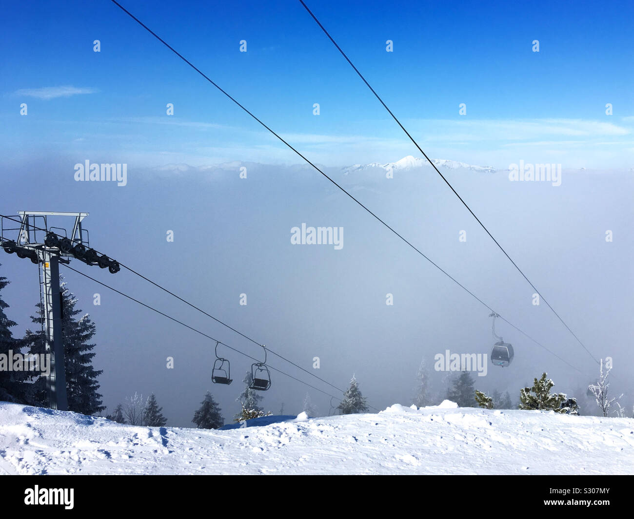 A Ski Cable Car Emerges From The Fog Above The Snow Covered