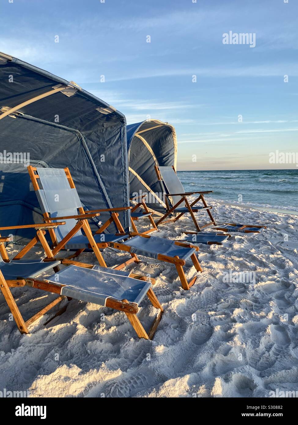 Blue beach tents and lounge chairs on white sand beach with water view Stock Photo