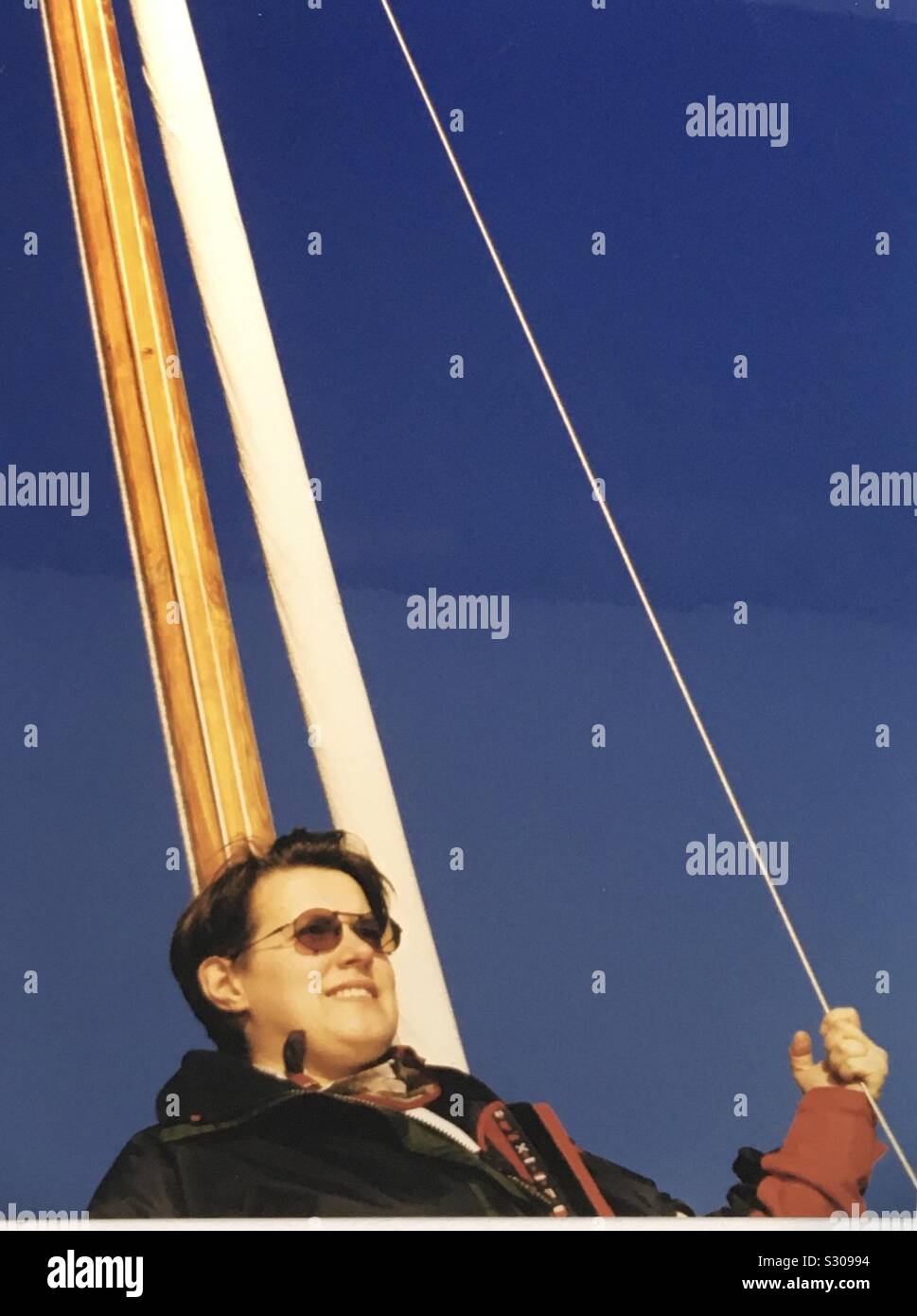 Frau steht am Mast eines Segelbootes und blickt in die Ferne Stock Photo