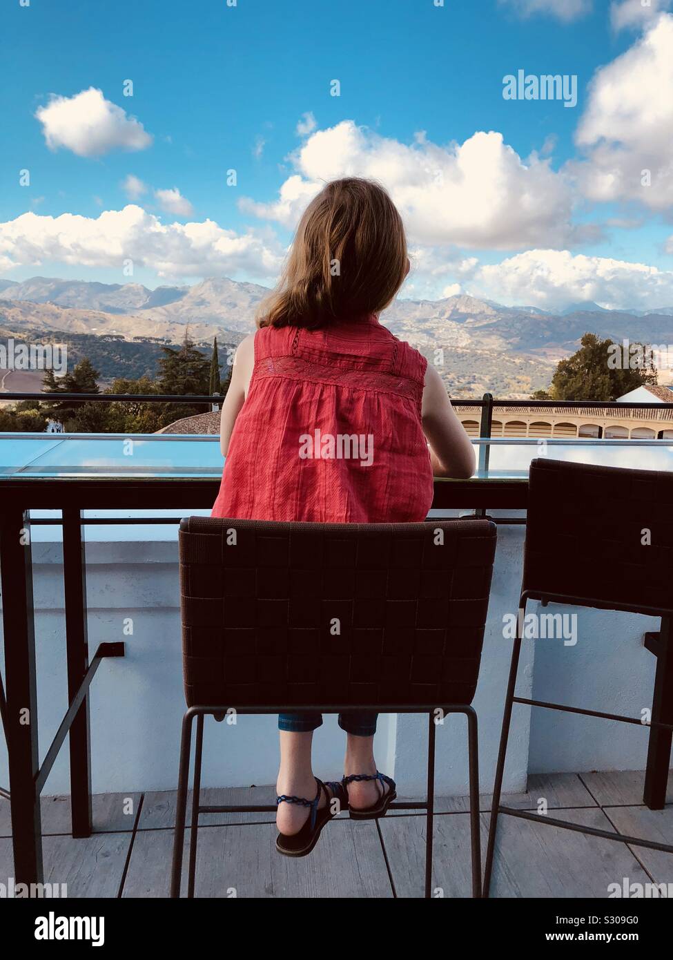 Rear view of girl sitting on a chair at the top of a building looking at the view - Smartphone Captured Stock Image