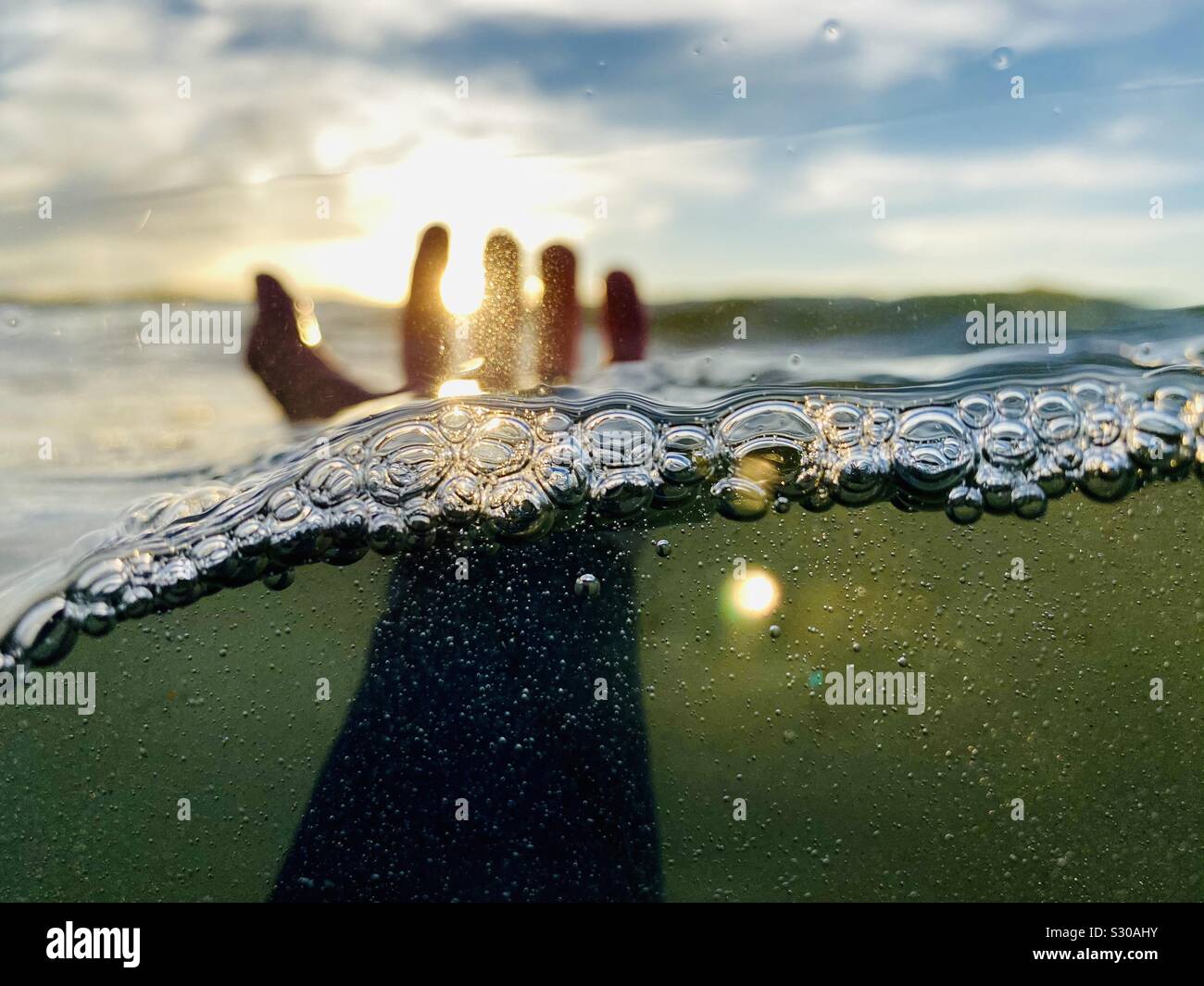A over-under photo of a left hand coming out of the water. Stock Photo