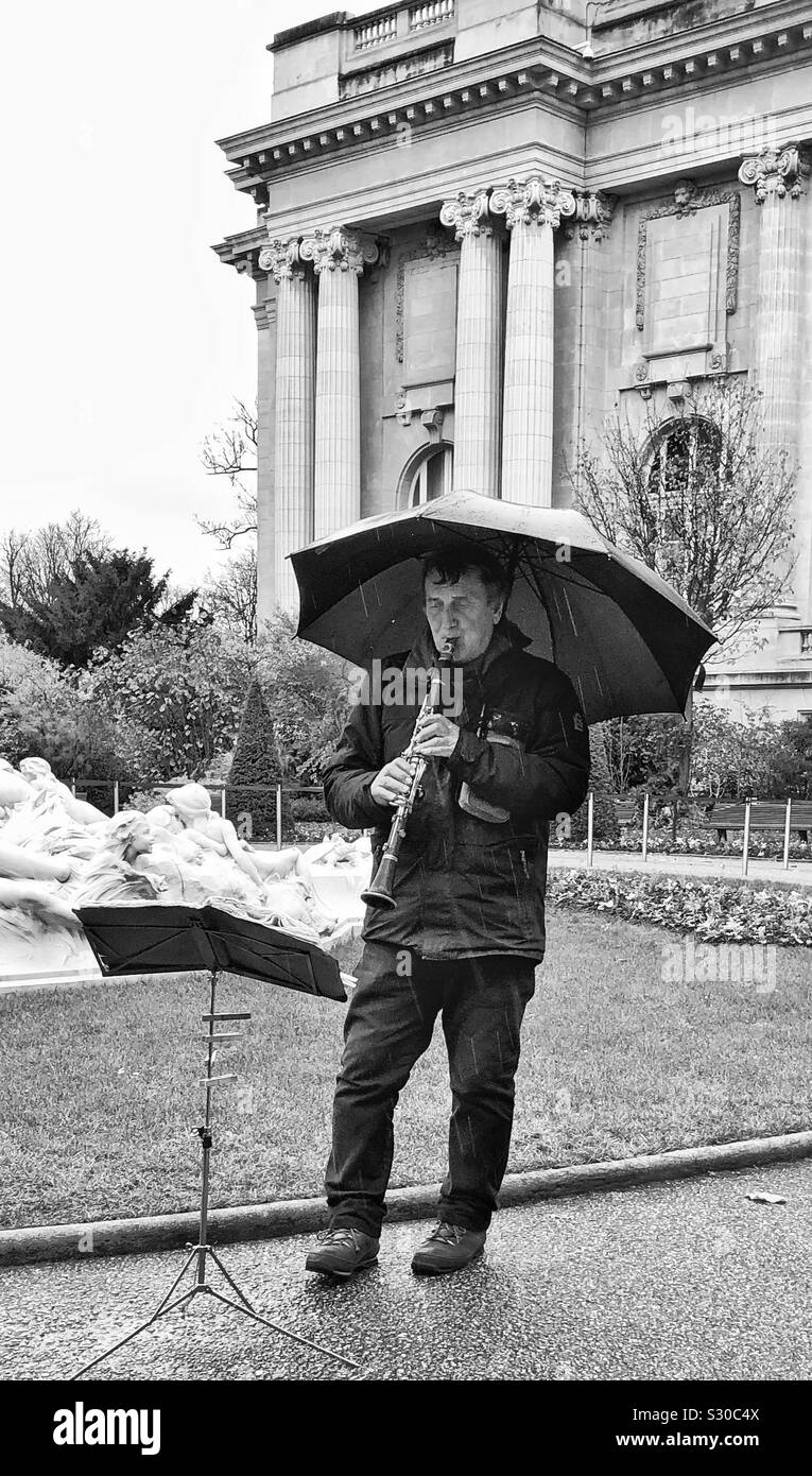 Clarinet player with umbrella plays in the rain outside the Grand Palais, Paris, France.  Black and white. Music stand in front of him. Stock Photo