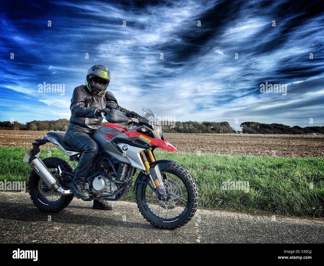 Female motorcyclist parked on remote countryside road on custom built bmw GS310 adventure motorcycle Stock Photo