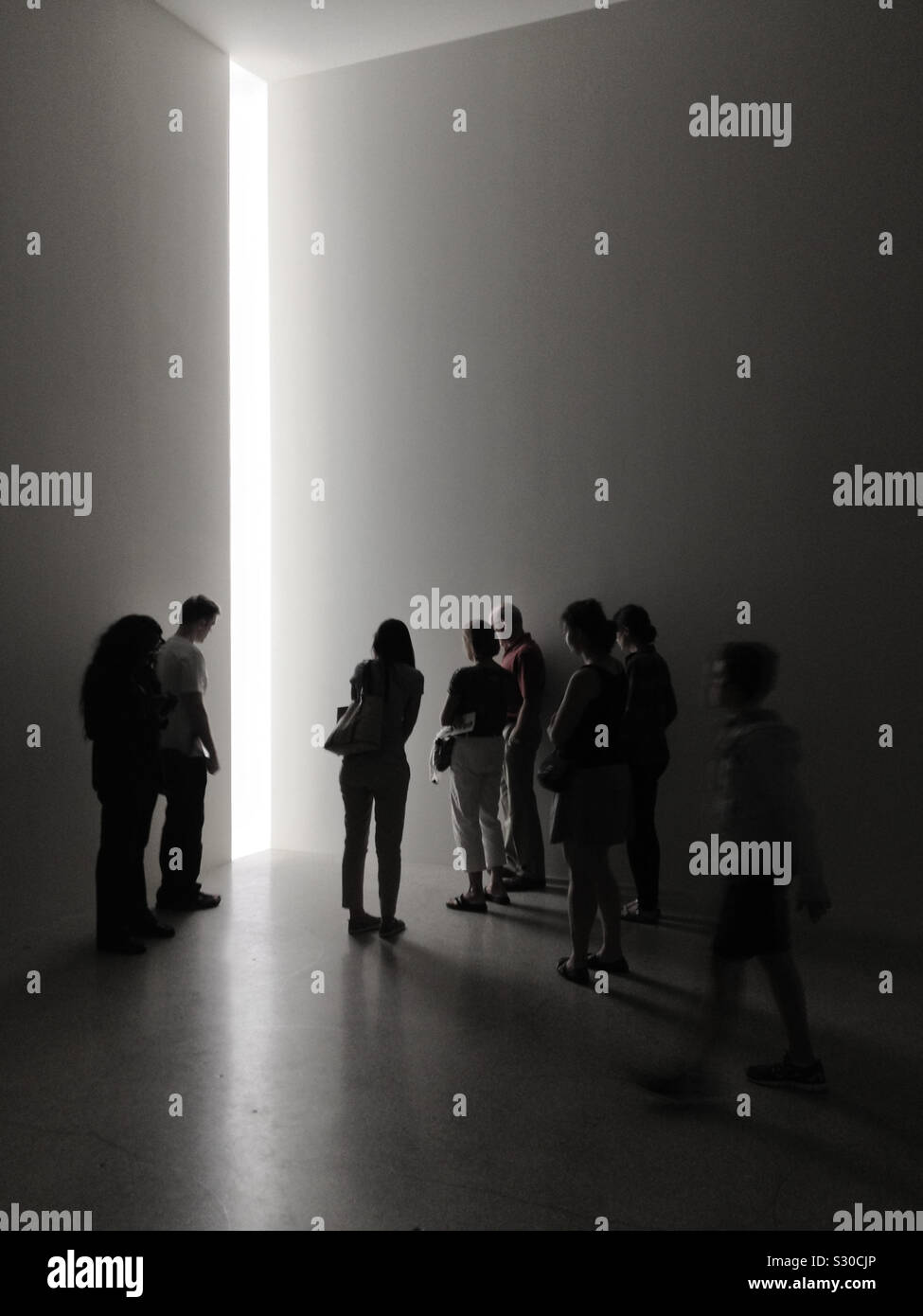 People standing around looking into a gap of light. Art exhibit. Concept. Stock Photo