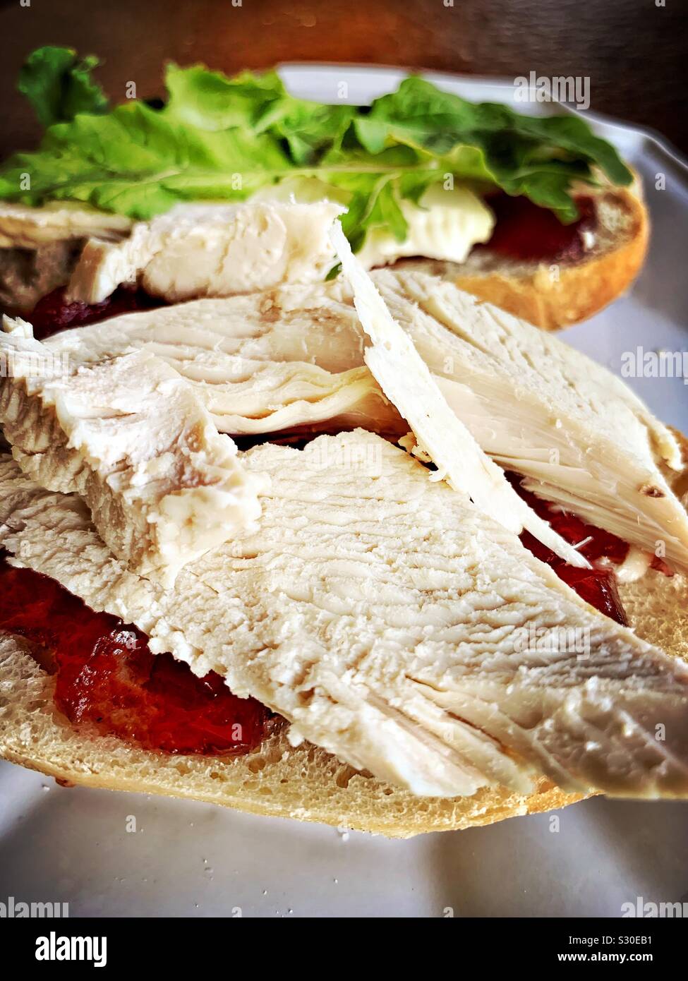 Leftover turkey is used to make a delicious sandwich with arugula, Brie cheese, and cranberry sauce. Stock Photo