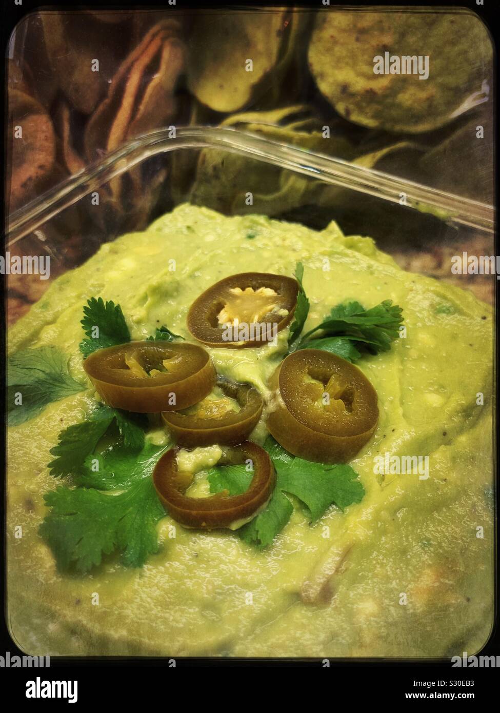 Guacamole is topped with pickled jalapeño rings and cilantro with chips in the background. Stock Photo