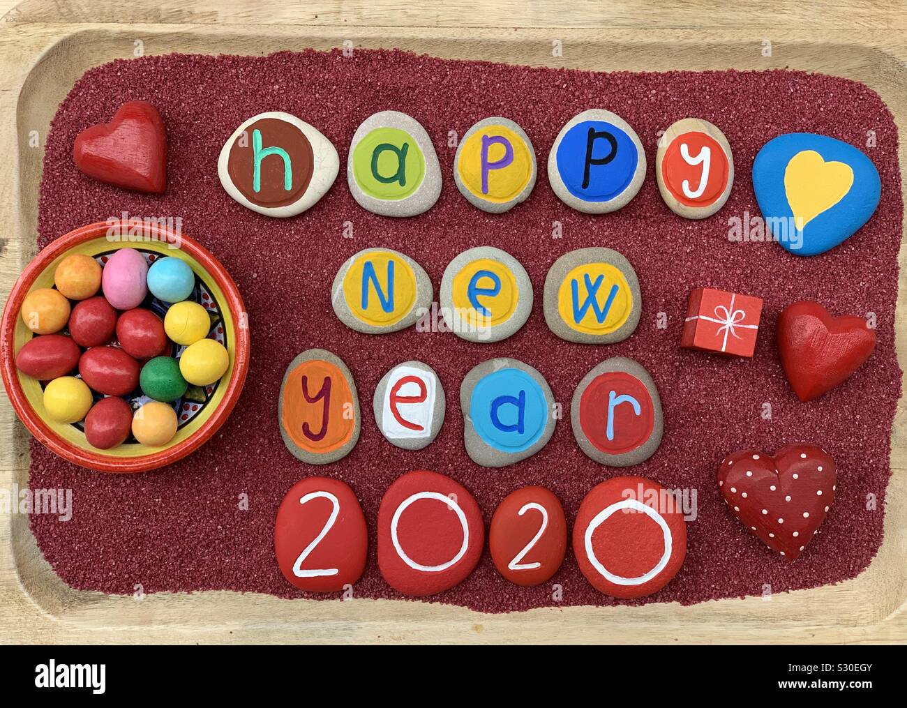 Happy New Year 2020 with a creative composition of multi colored stone letters over red sand Stock Photo