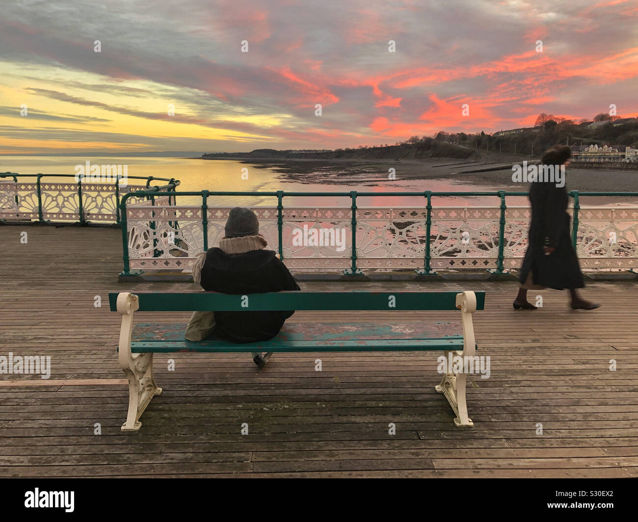 Two ladies on Penarth pier at sunset, walking and reading a book, South Wales, December. Stock Photo