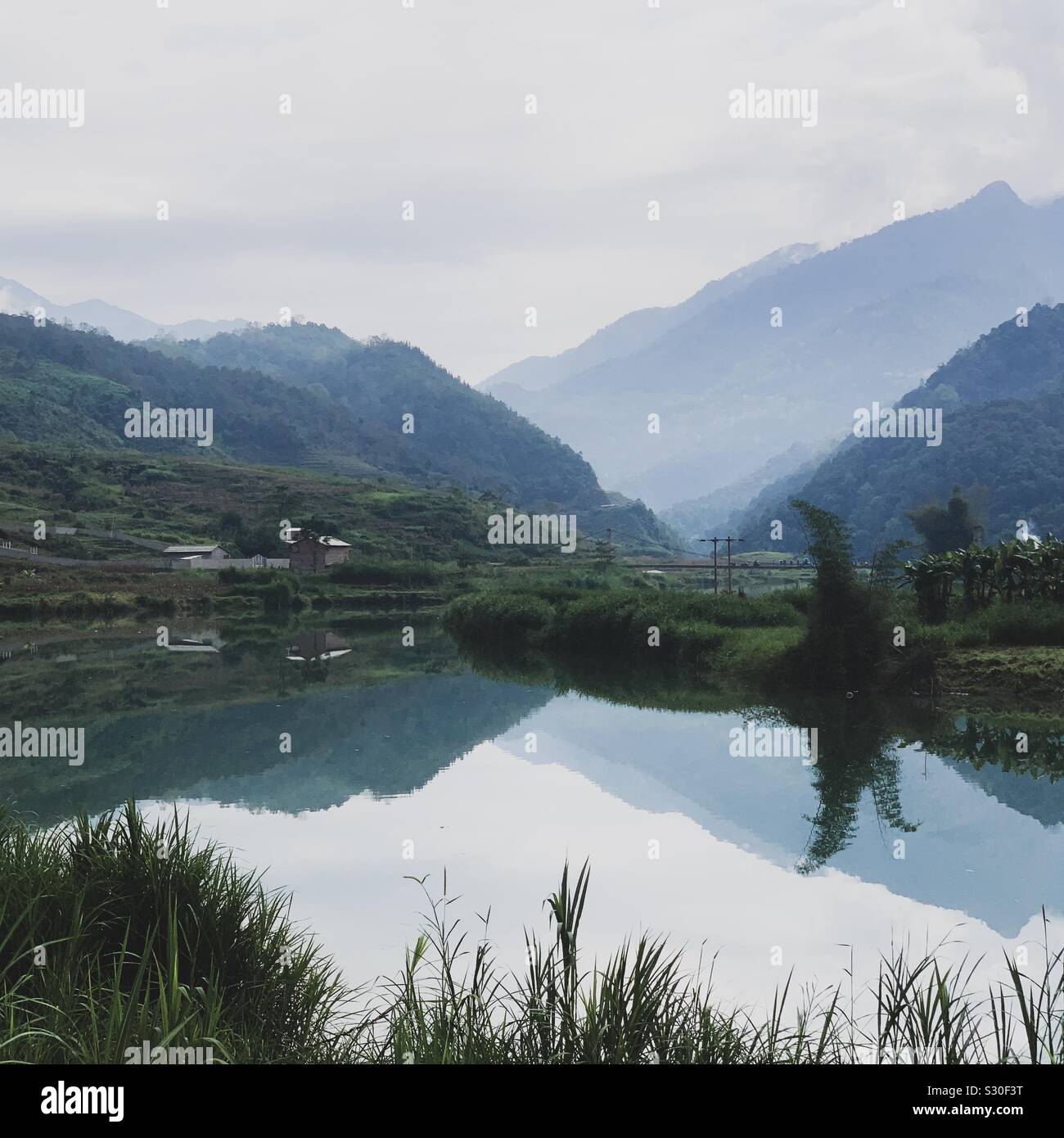 Reflections on Song Lo River in Quan Ba District, Ha Giang, Vietnam. Blue hues of mountain range with still glass like water. Near Song Mien village. Stock Photo