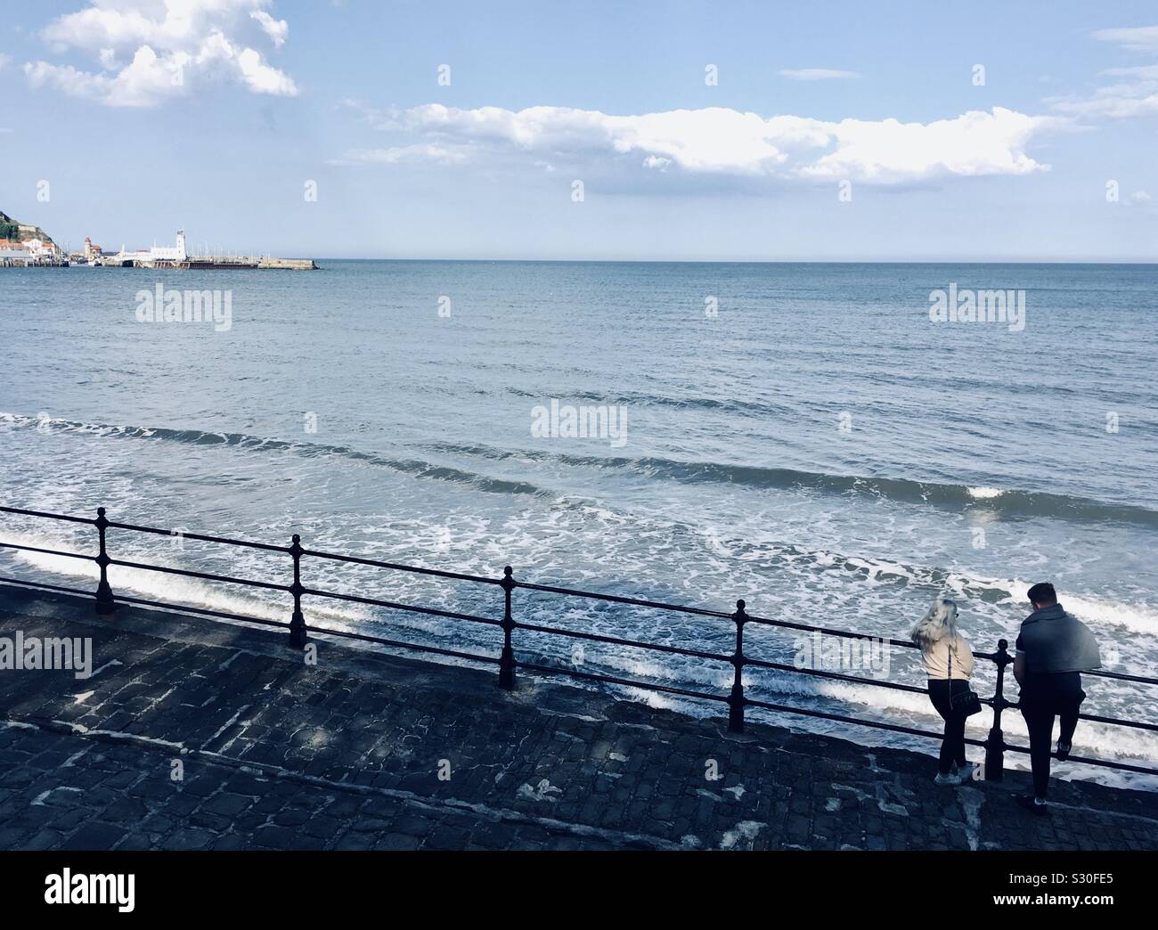 Couple looking over railings at Scarborough, Yorkshire coastline from the South Bay - Smartphone Captured Stock Image